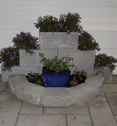 a blue potted planter sitting on top of a cement wall next to flowers