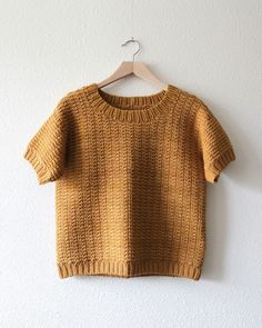 a brown sweater hanging on a wall next to a hanger with a white background