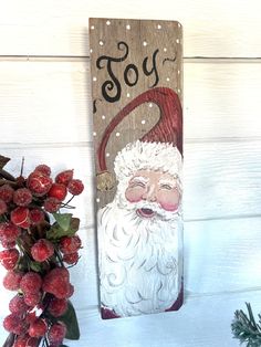 a wooden sign with a santa clause painted on it and berries in the foreground