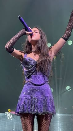 a woman in a purple dress holding a microphone up to her head while standing on stage