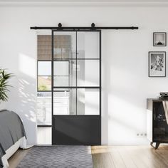 a bedroom with white walls and wooden flooring, black sliding glass doors to let in light into the room