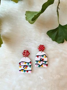 two colorful earrings sitting on top of a white fur covered floor next to a plant