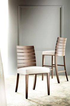 two wooden chairs sitting next to each other on a carpeted floor in front of a gray wall