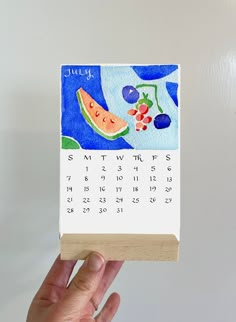 a hand holding up a calendar with watermelon and cherries painted on it