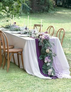 the table is set with purple flowers and greenery on it, along with candles