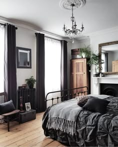 a bed sitting in a bedroom next to a window covered in black curtains and pillows