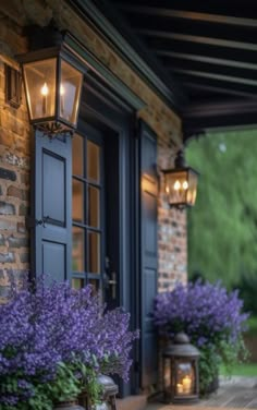 purple flowers in front of a house with two lanterns on the porch and one lantern lit up