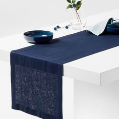 a blue table runner on top of a white table with two bowls and a vase