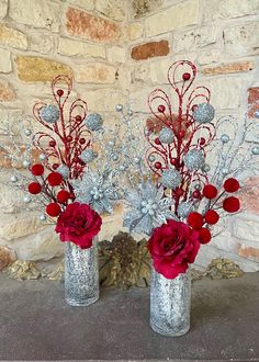 two vases with red flowers and silver branches in front of a brick wall,