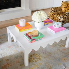 a white coffee table topped with books next to a leopard print chair and fire place