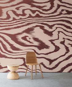 a wooden chair sitting in front of a wall with an abstract design painted on it