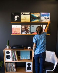 a woman standing in front of a desk with records on the wall and shelves above it