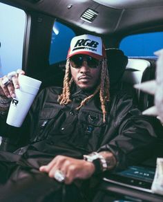 a man with dreadlocks sitting in the back of a car holding a cup