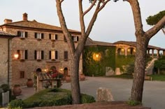 an old stone building with trees in the foreground and light shining on it's windows