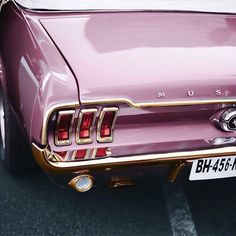 an old pink car parked in a parking lot next to another car with the license plate on it