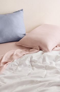 a bed with two pillows on top of it next to a white and blue pillow