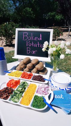 a table topped with plates and trays filled with different types of food next to a sign that says baked potato bar