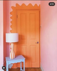 an orange door in a pink room next to a blue table with a lamp on it