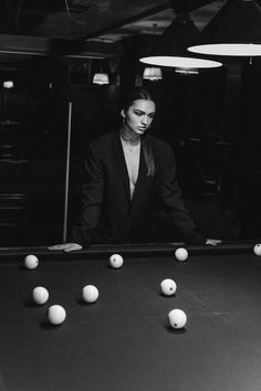 a black and white photo of a woman leaning over a pool table with balls in front of her