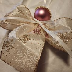 a pink ornament hanging from a ribbon on a white sheet with snowflakes