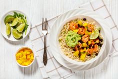 a white plate topped with rice and shrimp next to a bowl of mangoes, limes and avocado