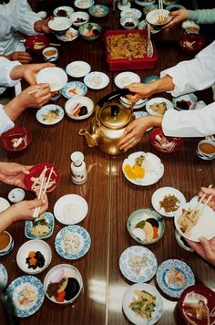 a group of people sitting around a wooden table eating food from bowls and plates with chopsticks