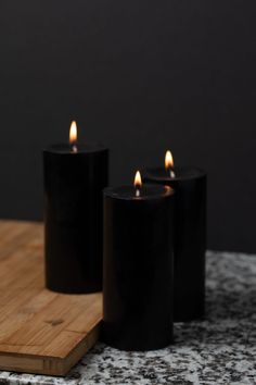 three black candles sitting on top of a wooden cutting board