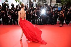 the back of a woman in a red dress walking on a red carpet with cameras surrounding her