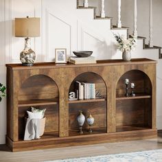 a wooden shelf with books, vases and pictures on it in front of stairs