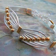 a close up of a metal bracelet on a stone surface with gold beads and silver wire