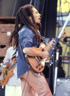 a man with dreadlocks plays an electric guitar at a music festival on stage