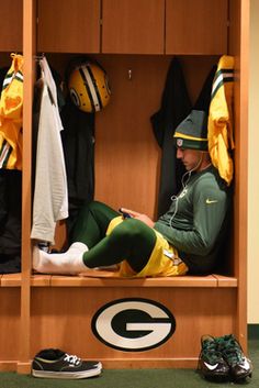 a green bay packers player sits in the locker room with his team's gear