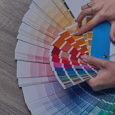 a person holding a pantoner and color swatches in their hands, on top of a wooden table