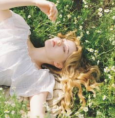 a woman laying in the grass with her eyes closed and hands behind her head, wearing a white dress