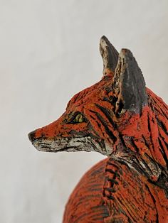 an orange and black statue of a fox on a white wall behind it's head