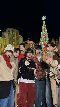 a group of young people standing next to each other in front of a christmas tree