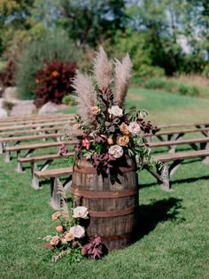 a wooden barrel with flowers on it sitting in the middle of a field next to rows of benches