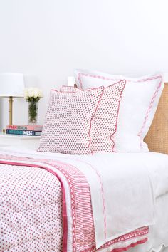 a bed with white sheets and pink trimmings on it, next to a night stand