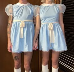 two women dressed in blue dresses standing next to each other with tattoos on their arms