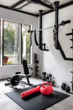 Home gym with exercise equipment, including a rowing machine, kettlebells, weights, and a barbell rack, near large windows. Home Gym Setup Overstock, Black Gym Room At Home, Dark Home Gym Aesthetic, Bedroom With Gym Equipment, Gym Equipment Storage Loft, Rubber Floor Tiles