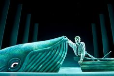 a man sitting on top of a boat next to a giant blue whale