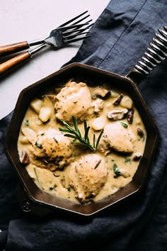 a skillet filled with chicken and dumplings on top of a blue cloth next to two forks