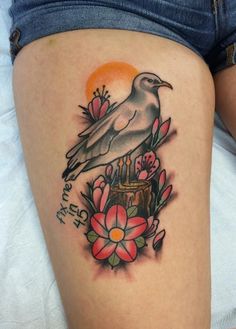 a bird sitting on top of a tree stump with flowers around it and the sun in the background