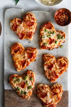 several heart shaped pizzas on a tray with sauce and seasoning next to them