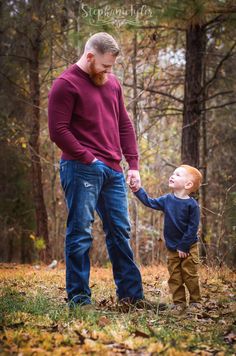 a young boy holds the hand of his father as they stand in front of some trees