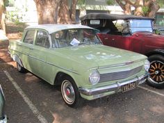 an old green car parked in a parking lot