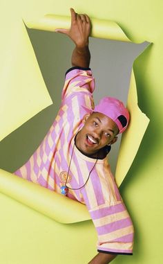 a man with headphones on standing in front of a yellow wall and pointing to the side