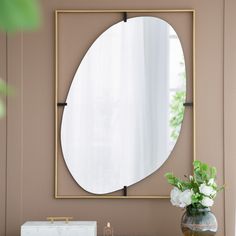 a mirror on the wall above a table with a vase and flowers in front of it