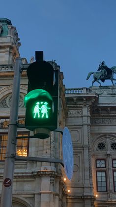 a green traffic light sitting in front of a tall building with a horse and rider on it