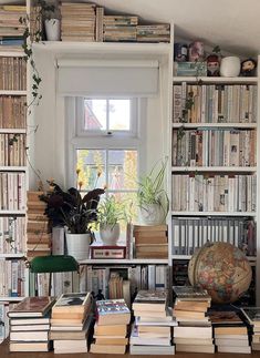 a room filled with lots of books on top of a wooden table next to a window